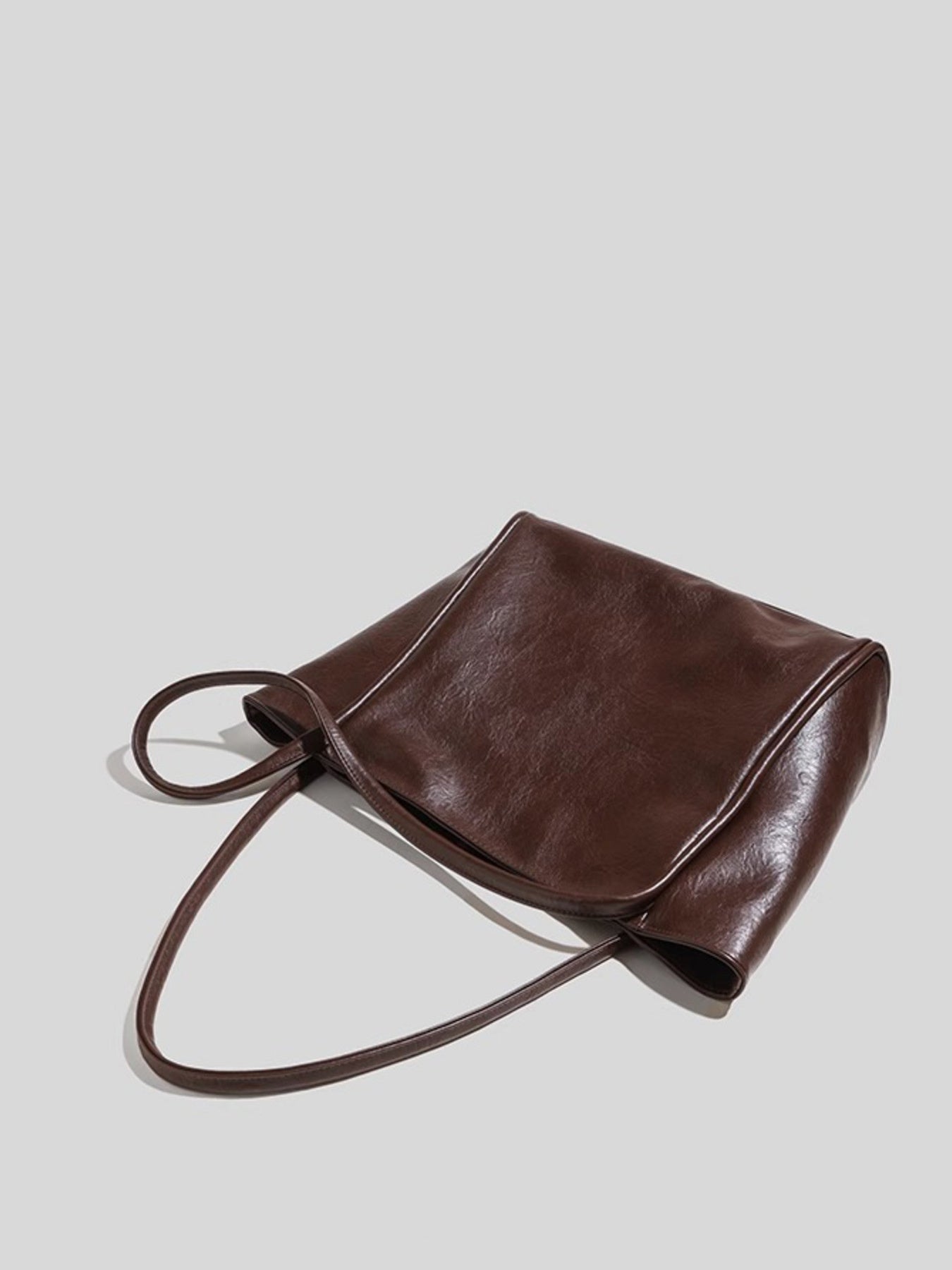 Brown leather handbag on a light gray background, shows drape of handles