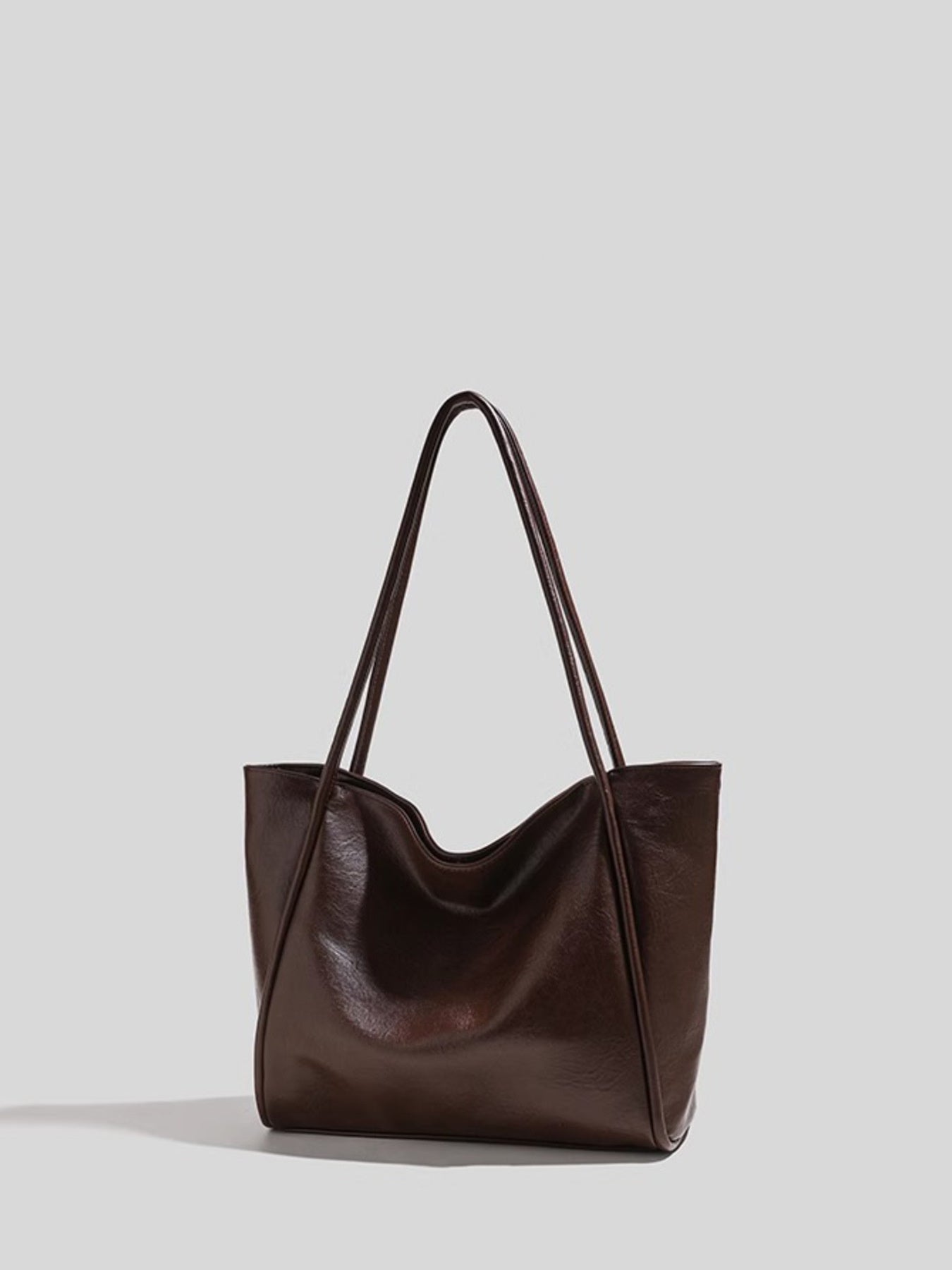 Brown leather tote bag on a light gray background showing texture in light